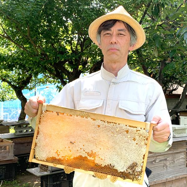 「森を守る蜂の話」の店主、養蜂家の山口朝さん。西荻窪の農園にある巣箱の前で